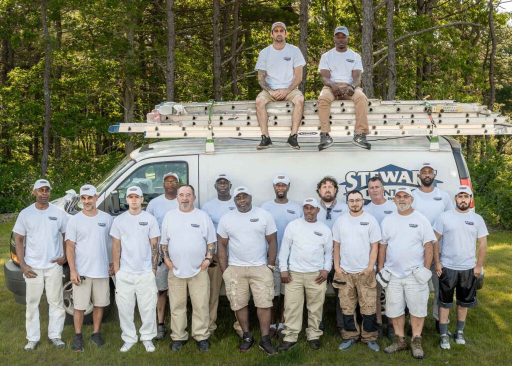 Fifteen crew and job leaders standing in front plus two sitting on top of the Stewart Painting work van.