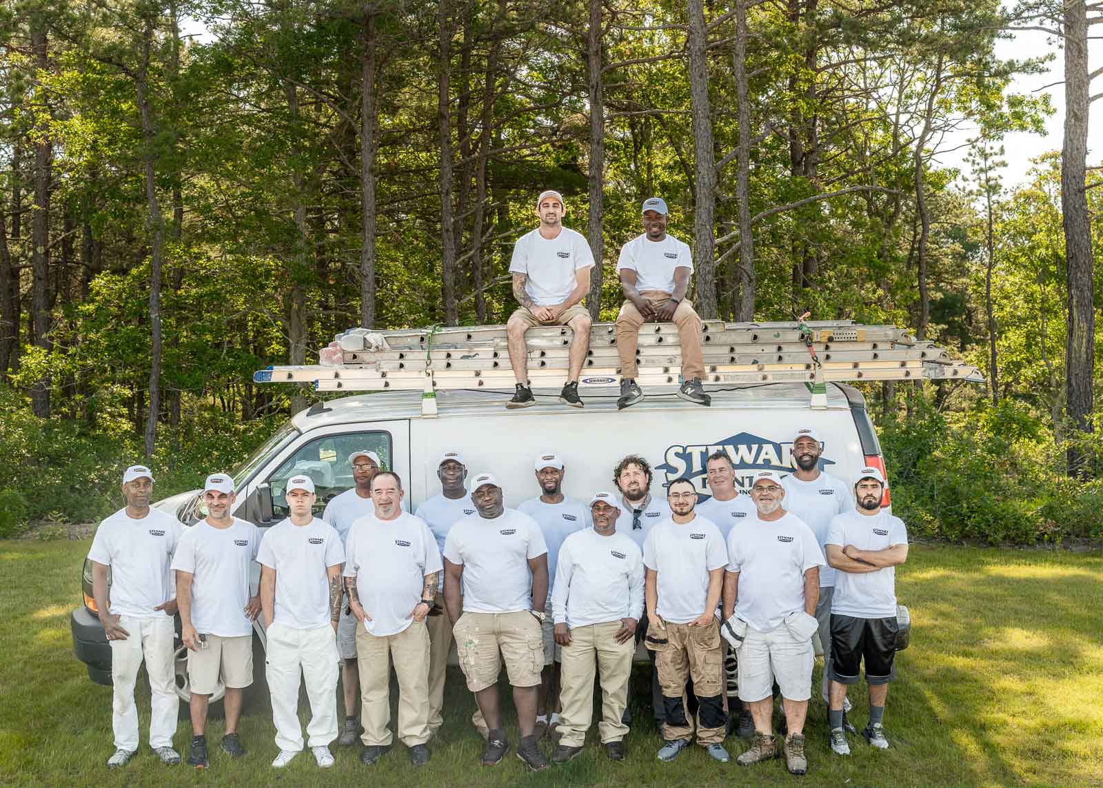 Fifteen crew and job leaders standing in front plus two sitting on top of the Stewart Painting work van.