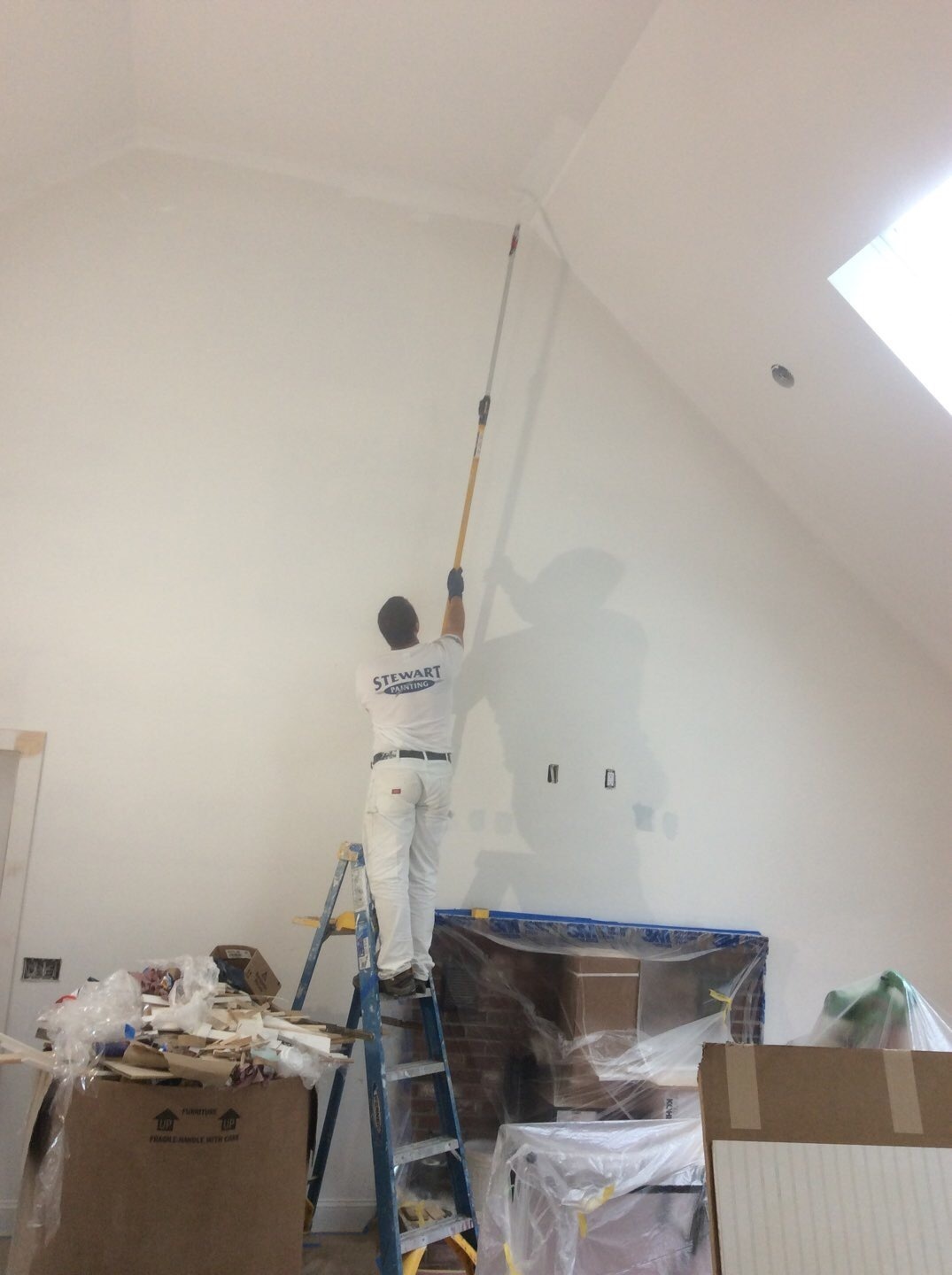 Painter on ladder using roller on extension to paint Cathedral Ceiling