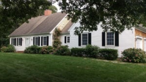 House painted white with black shutters surrounded by greenery